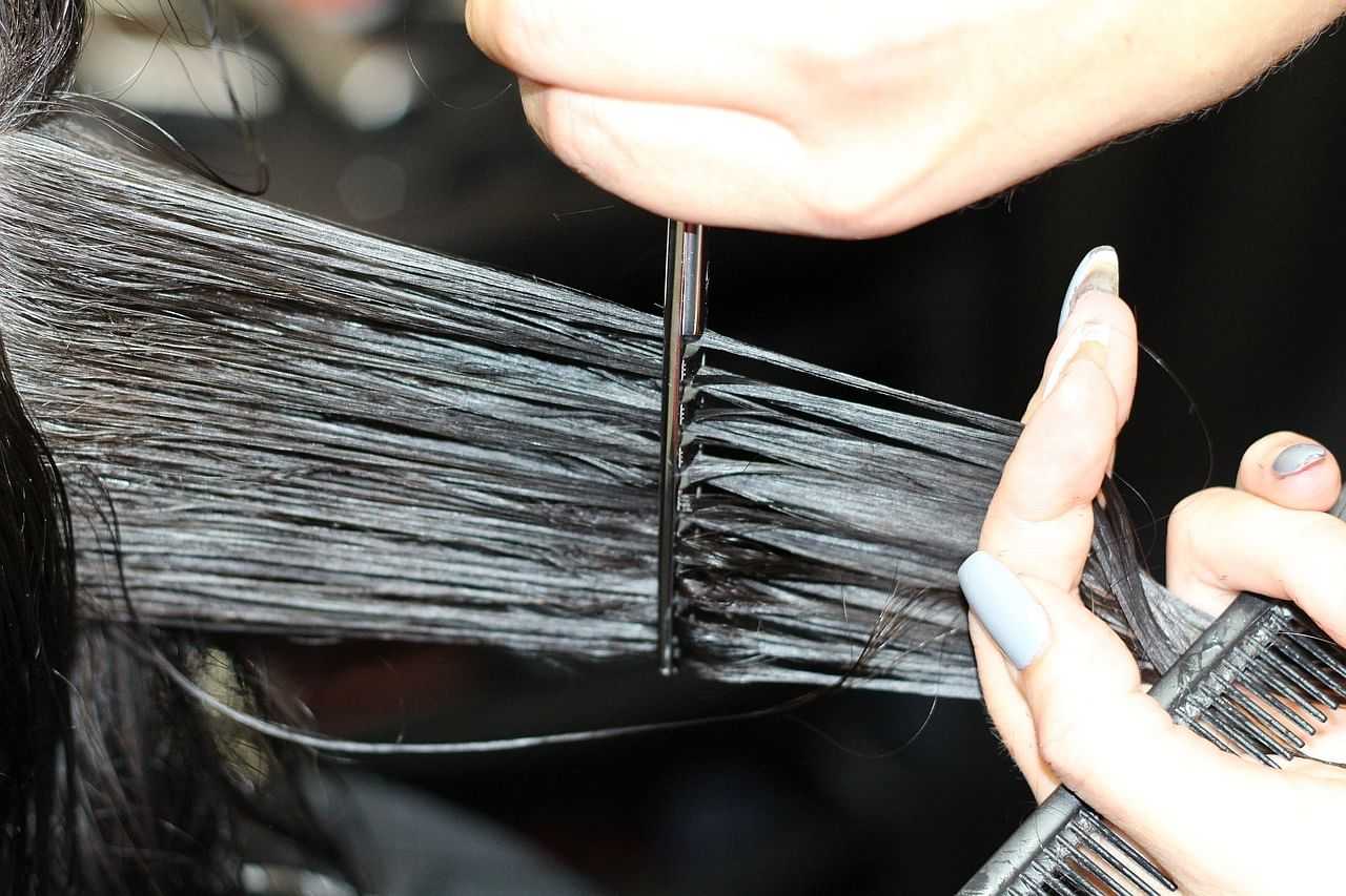 Hairstylist cutting wet, dark hair with scissors in a close-up shot.